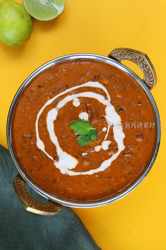 金属卡达伊碗的图像包含自制的Dal makhani(黑扁豆和红芸豆咖喱)餐，灰色的平纹棉布，全柠檬和半柠檬，黄色背景，高视野